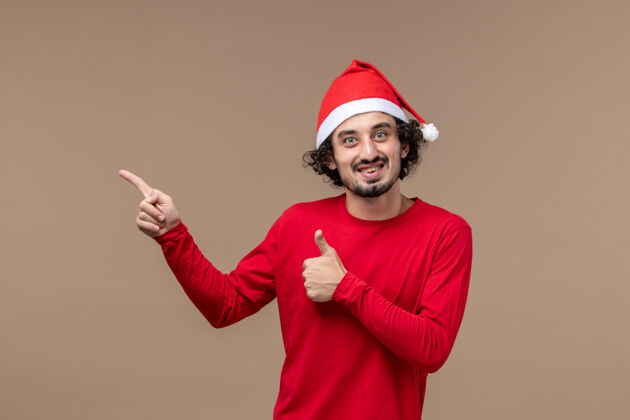 帽子正面图棕色办公桌上穿着红色圣诞斗篷的年轻男性情感节日圣诞节观点棕色乐趣