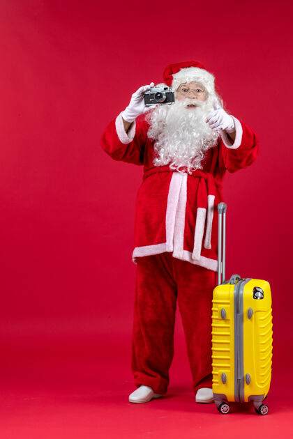 节日红墙上带黄包的圣诞老人用相机拍照的正面图圣诞老人人圣诞