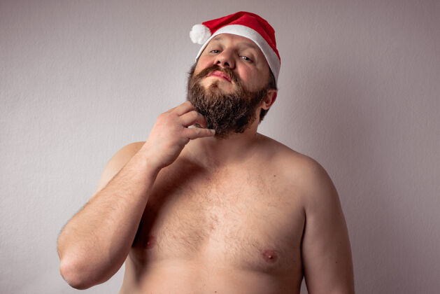 衣服特写镜头一个赤膊胡须男子戴着圣诞老人的帽子在灰色的背景看胡须水平