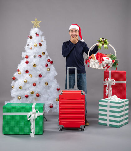 抱着在灰色的圣诞树旁 戴着圣诞帽的年轻人手里拿着礼品篮 高兴极了圣诞树灰色男人