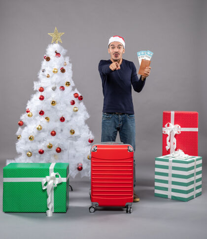 礼物惊讶的人拿着他的旅行票 指着灰色的东西尖包圣诞