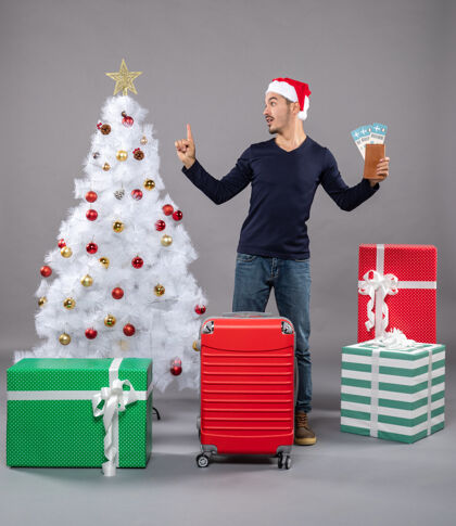 圣诞树一个带着红色手提箱的惊讶男人拿着灰色的旅行票圣诞帽灰色庆祝