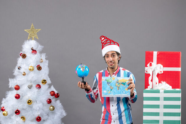 有趣前视图微笑的人拿着世界地图和地球仪假期圣诞帽礼品盒