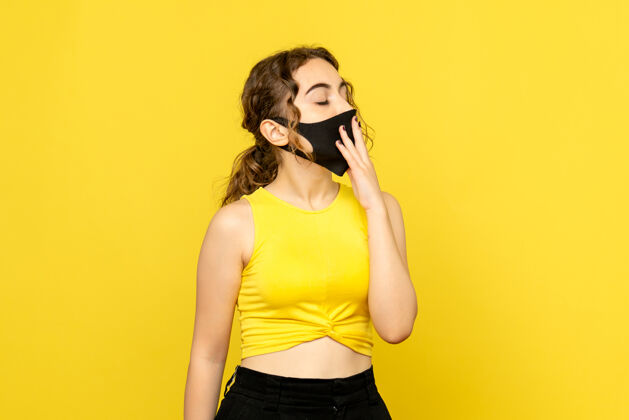 女性黄色墙壁上戴着黑色面具打哈欠的年轻女子的正视图年轻女性人物年轻