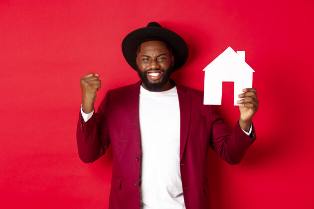 胡须房地产快乐的黑人男子欢呼雀跃 展示纸家居用品 站在红色背景上男人年轻促销