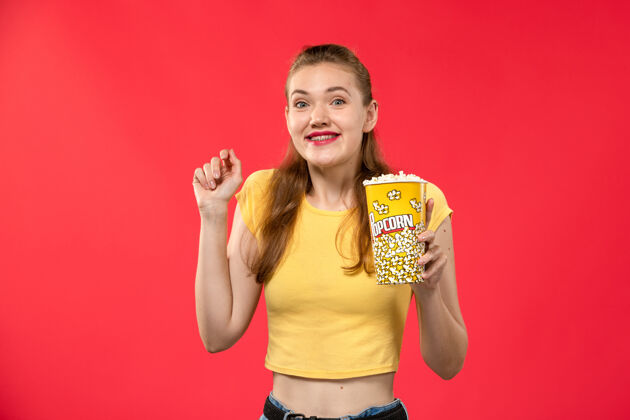漂亮正面图年轻女性在电影院拿着爆米花在红面电影院看女性趣味电影电影爆米花观点