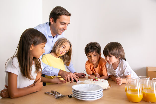 白种人微笑的父亲正在为孩子们切美味的生日蛋糕可爱的孩子们站在桌子旁 一起庆祝生日 等待甜点童年 庆祝和节日的概念蛋糕孩子玩耍