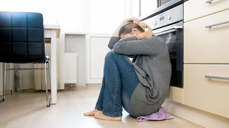 悲伤年轻的女人在厨房的地板上哭泣家庭关系问题和抑郁劳累家务保护