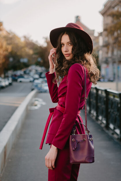 年轻穿着紫色西装的漂亮时髦女人走在城市街头 春夏秋冬时节时尚潮流戴着帽子 手拿钱包服装配饰魅力