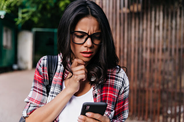 严重一个戴着眼镜 晒得黝黑的女人站在街上拿着电话漂亮严肃的女孩读着短信拉丁享受街道
