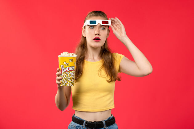 爆米花正面图年轻女性在电影院拿着爆米花戴着d太阳镜在红墙电影院看电影女性的颜色剧院女性漂亮