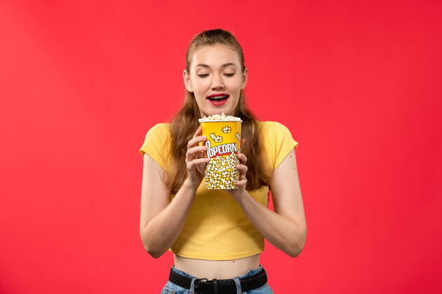 身体前视图年轻女性在电影院拿着爆米花包在浅红色的墙上看电影剧院爆米花摆姿势