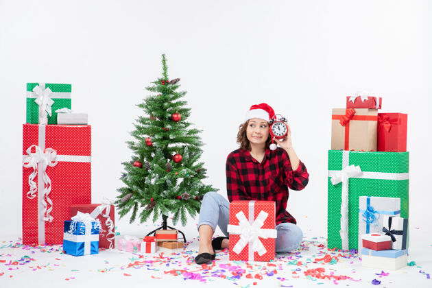 时钟前视图年轻女子坐在圣诞礼物周围拿着白色墙上的时钟女人快乐十二月