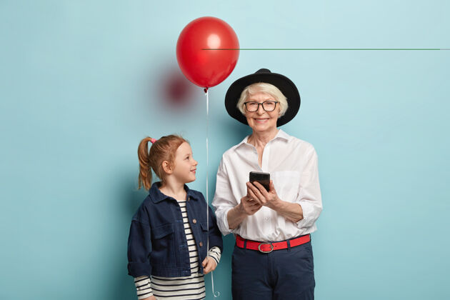 成熟快乐的老太太在网上聊天 总是保持联系 穿着时髦的服装迷人的红头发女孩马尾辫 手持红气球 祝贺奶奶周年生日空闲时间手机孙子