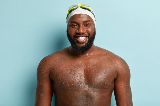 裸体这张照片是一位皮肤黝黑 笑容灿烂 牙齿洁白 在蓝色背景下裸体的非洲裔男性水滴男性护目镜