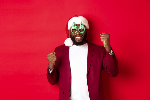 肖像圣诞快乐快乐的黑人戴着滑稽的聚会眼镜和圣诞帽庆祝圣诞老人自信