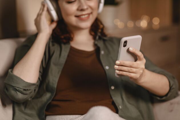 年轻人女人用现代耳机和智能手机设备在家里的沙发上人电子产品耳机