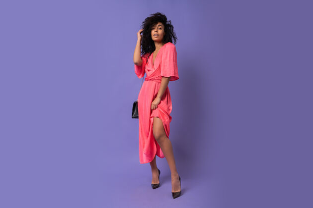 女性穿着粉色派对礼服的漂亮黑人女人在紫色的墙上摆姿势穿高跟鞋全长度女人幸福蓝色