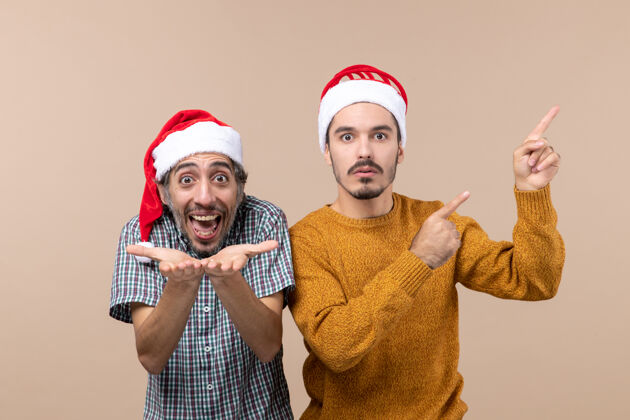 脸前视图两个戴着圣诞帽的男人都在孤立的背景上展示了一些东西两个男人男人显示