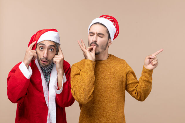 前面正面图两个戴着圣诞帽的朋友一个在米色背景上制作厨师亲吻标志肖像两个脸