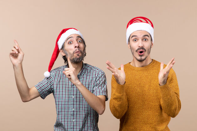 伙计们前视图两个戴着圣诞帽的惊讶的家伙一个展示了一些东西 另一个在孤立的背景上令人震惊惊奇帽子肖像