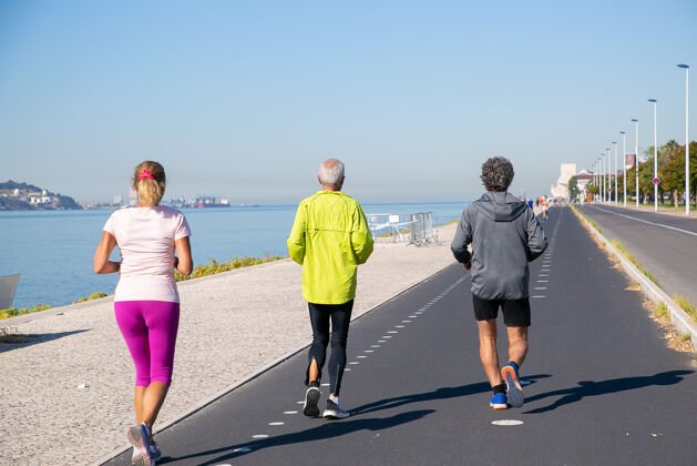 成熟穿着运动服 沿着河岸慢跑的成年人的后视图全长退休或积极的生活方式概念友谊老年人社区