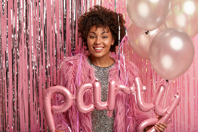 女人快乐女人的横拍庆祝特殊场合 生日或毕业 手持气球 穿着时髦的衣服 模特靠着粉色的墙壁用金属丝节日概念高兴闪亮单色