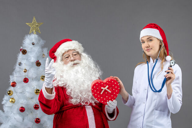 女性圣诞老人的正面图 灰色的墙上有女医生拿着礼物圣诞老人服装健康