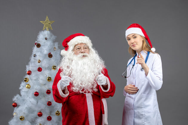 圣诞快乐圣诞老人和年轻女医生在灰色墙壁上的正视图服装年轻医疗