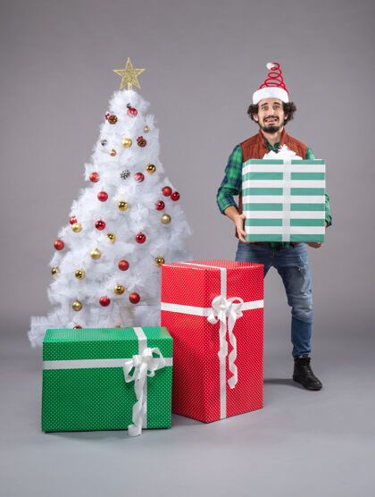 圣诞老人在灰色地板上的节日礼物周围的年轻男性周围圣诞帽礼物