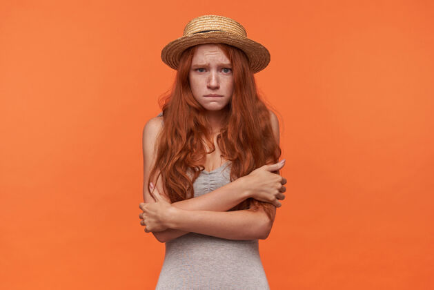 年轻摄影棚里的一张照片 一个年轻漂亮的红发女人被吓坏了 双手交叉站在橙色背景上 惊恐地看着镜头 额头皱了起来衬衫红发手臂