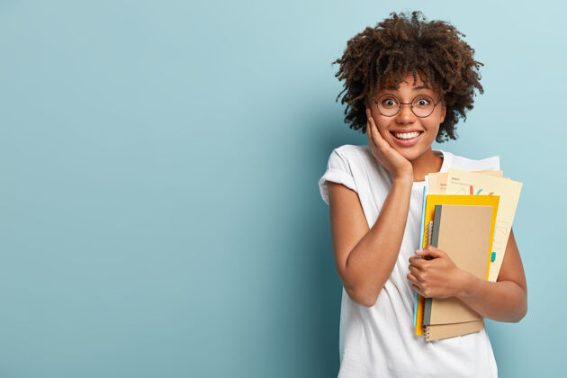 理发长相讨人喜欢的美国黑人妇女拿着笔记本 论文 在大学里学习 很高兴完成学业文案头发螺旋