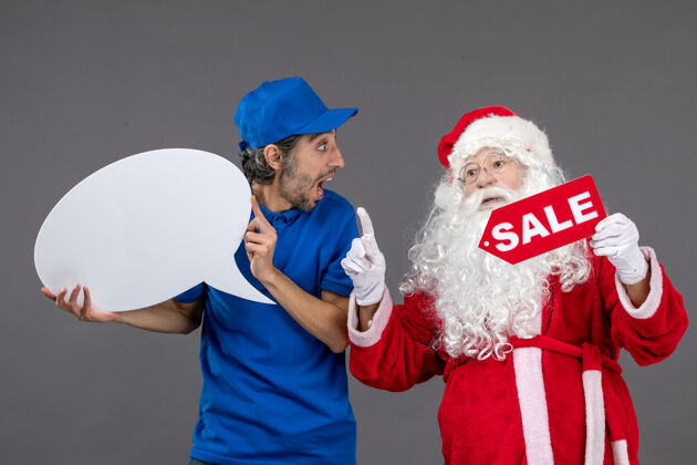 男圣诞老人与男信使手持白色标志和灰色墙上的销售横幅的正面视图圣诞老人男人前面