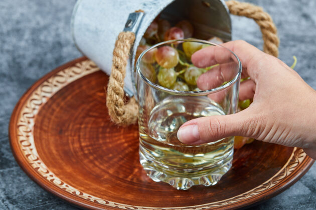 酒手拿一杯白葡萄酒和一小桶葡萄放在大理石背景上高质量的照片手盘子冰