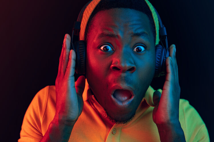 人年轻帅气快乐的时髦男人在霓虹灯下用耳机在黑工作室听音乐迪斯科舞厅 夜总会 嘻哈风格 积极的情绪 面部表情 舞蹈概念年轻表演享受