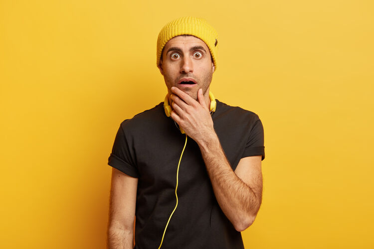 T恤年轻痴迷的家伙摸着下巴 瞪着的眼睛 不敢相信会有惊人的缓和 说不出话来惊讶恐惧情感