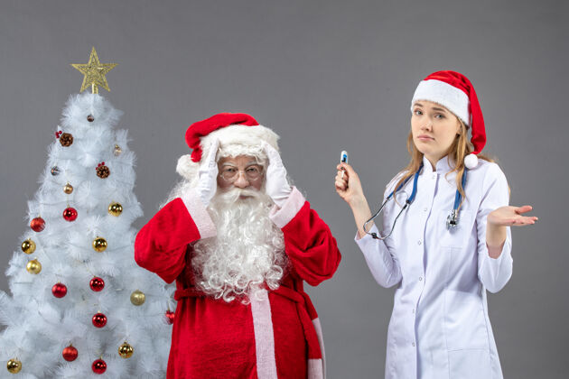 圣诞老人圣诞老人和女医生的前视图 女医生在灰色的墙上拿着测温仪女十二月测量