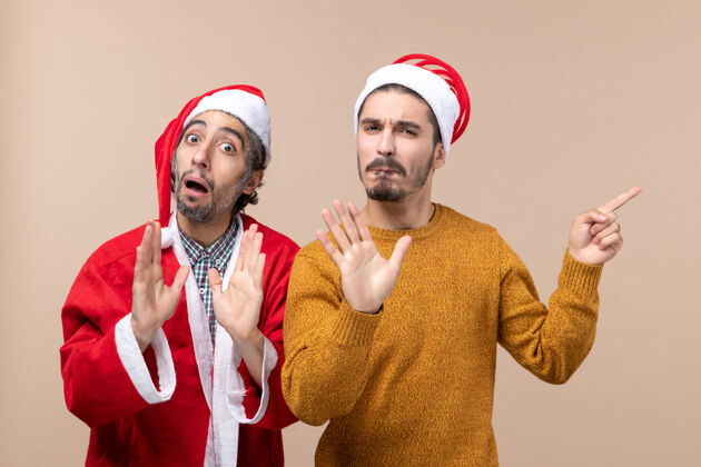 风景正面图两个戴着圣诞帽的朋友在米色孤立的背景下出人意料两个朋友帽子朋友