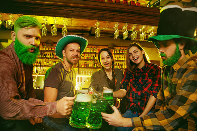 柜台圣帕特里克节派对快乐的朋友在庆祝和喝绿色啤酒年轻男女戴着绿色帽子酒吧内部啤酒杯子圣徒