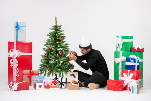人年轻人围坐在节日礼物装饰在白色墙上的小树的前视图圣诞花束人