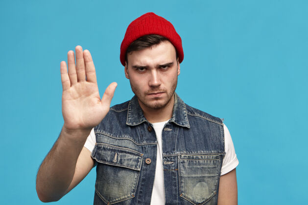 禁止肢体语言一个戴着红帽子的时尚年轻人的孤立镜头 显示出负面反应人室内年轻