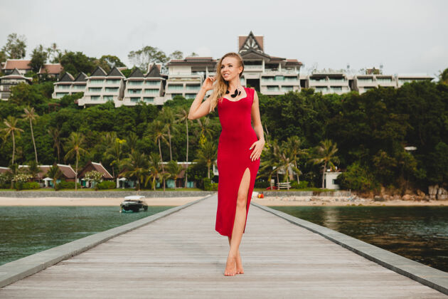美腿年轻漂亮迷人的女人独自站在豪华度假酒店的码头上 暑假 红色长裙 金色头发 性感服装 热带沙滩 诱惑 性感 微笑女孩海洋礼服