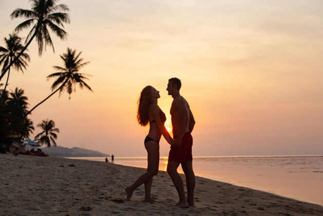 海洋年轻性感浪漫的情侣在夕阳下相爱 在夏日的沙滩上快乐地穿着泳衣一起玩夏天浪漫乐趣