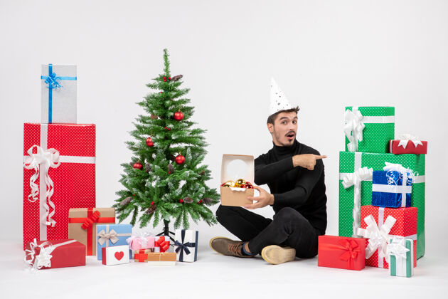 包装正面图：年轻人围坐在节日礼物旁边 手里拿着白色墙上的玩具包快乐玩具前面