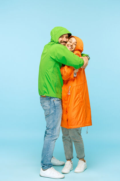 季节这对穿着秋夹克的年轻情侣在摄影棚里惊艳地隔离在蓝色上人类快乐的积极情感寒冷天气的概念男女时尚的概念人惊讶寒冷