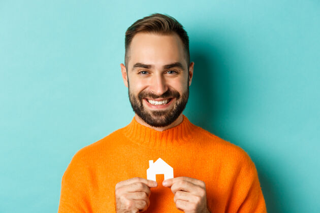 成人房地产概念快乐的年轻人寻找房屋租金 抱着纸房子微笑摆姿势男人风格