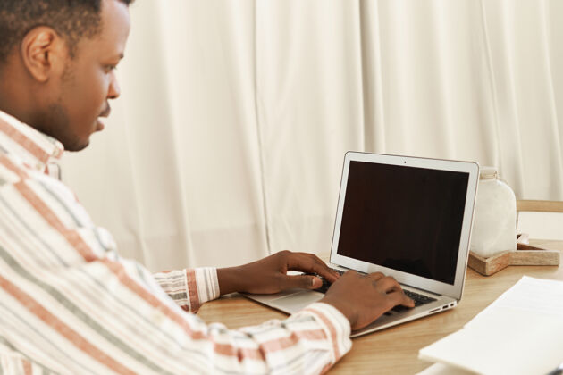 男人严肃的黑皮肤年轻人在家里用键盘在黑屏便携式电脑上工作技术休闲现代
