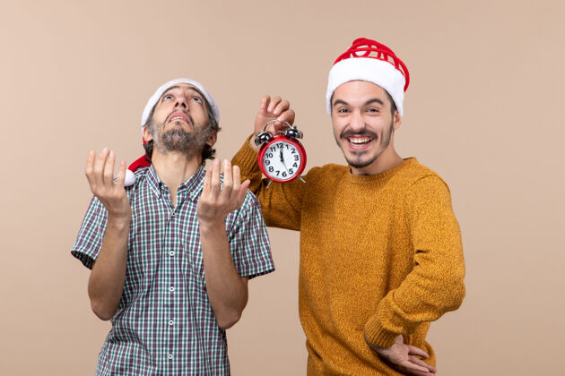拿着前视图两个圣诞老人一个张开双手看着天花板 另一个拿着闹钟 背景是米色的打开闹钟两个