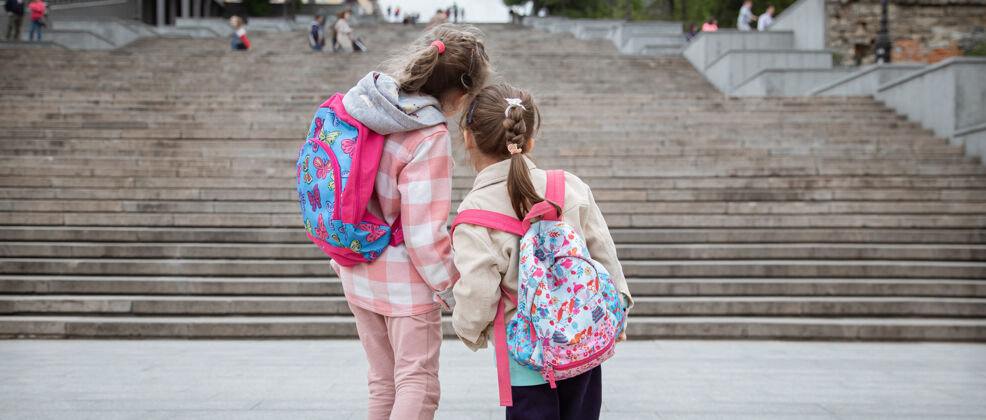 背包两个背着漂亮背包的小女孩手牵手一起上学童年友谊的概念女生学校散步