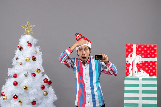 人前视图失望的男子与信用卡站在白色圣诞树附近圣诞快乐男性